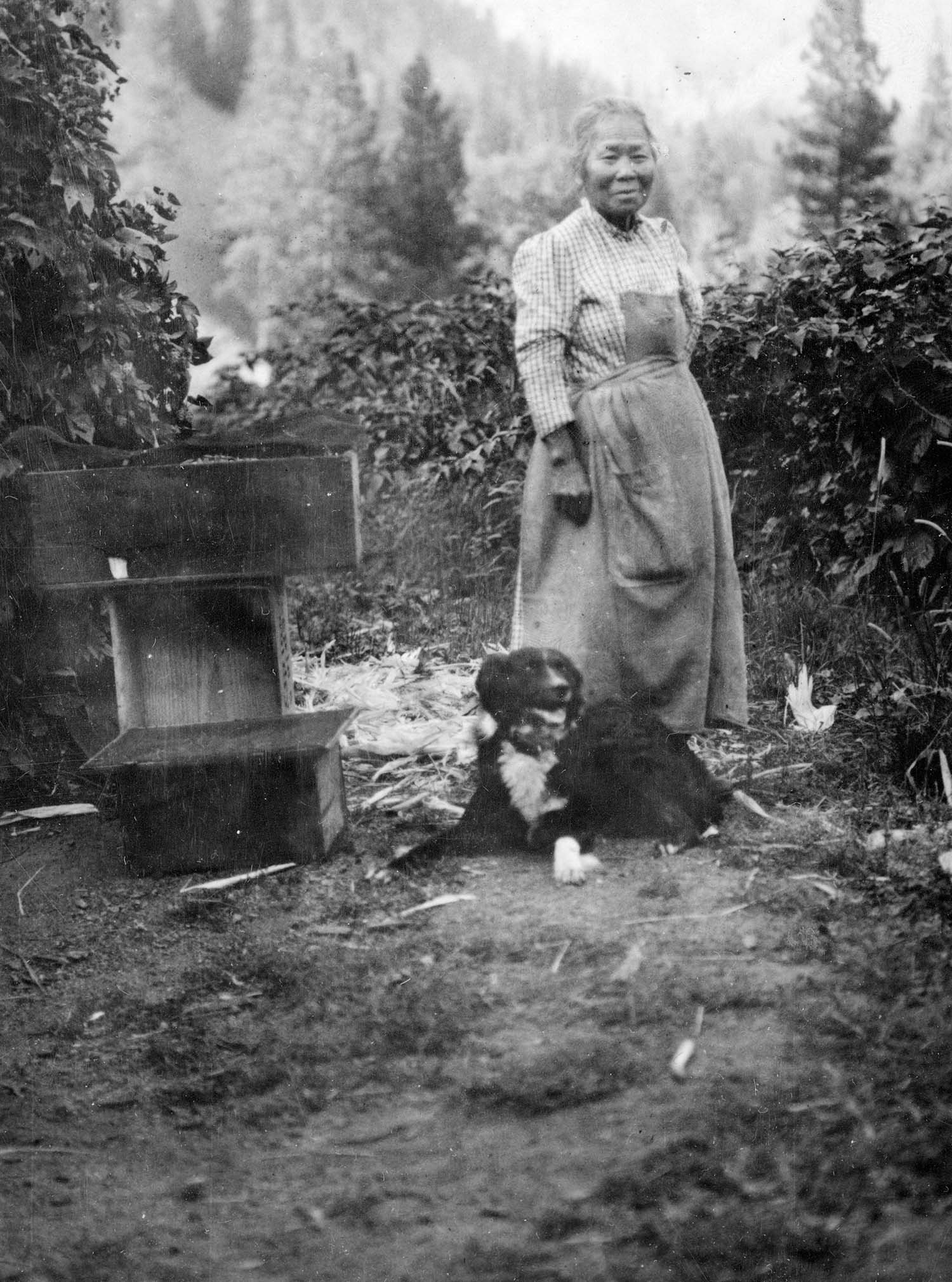 A black-and-white photo of Polly Bemis and a black dog standing outside.